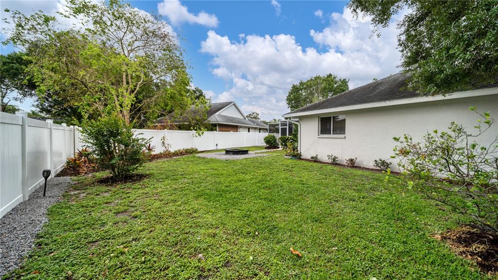 A backyard with a green lawn, a fire pit, and a white vinyl privacy fence — 5219 INVERNESS DRIVE, SARASOTA, FL
