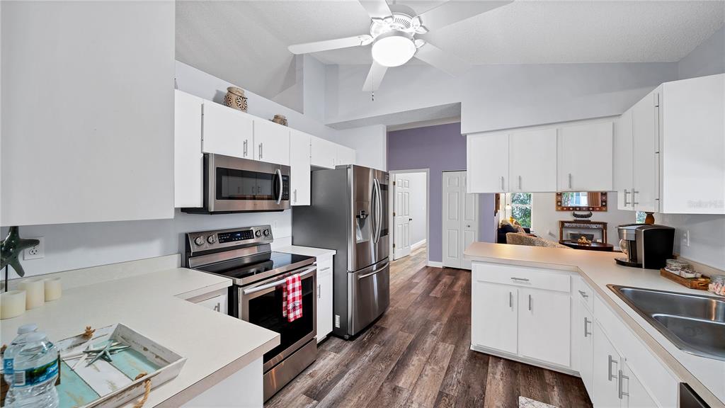 A kitchen features white cabinets, stainless steel appliances, and wood-look flooring under a ceiling fan — 5219 INVERNESS DRIVE, SARASOTA, FL