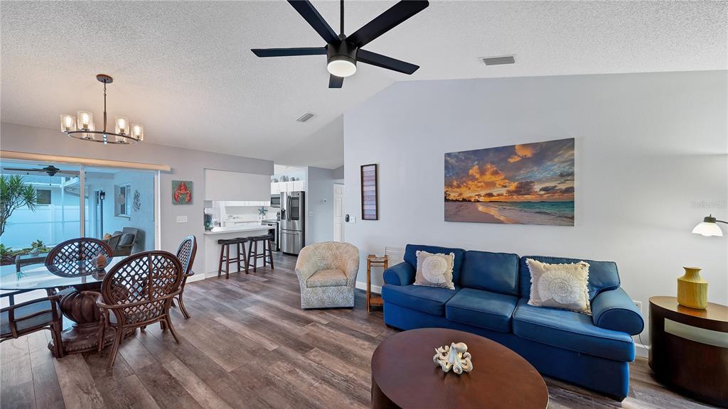 A living room and dining area feature wood-look flooring, a blue sofa, and ceiling fans — 5219 INVERNESS DRIVE, SARASOTA, FL