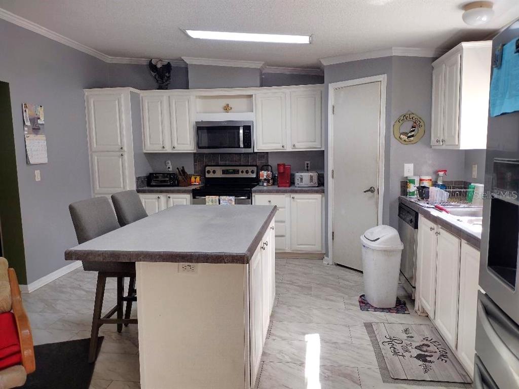 A kitchen features white cabinets, a central island with seating, and light-colored tile flooring — 1558 CANDLEBERRY STREET, BUNNELL, FL