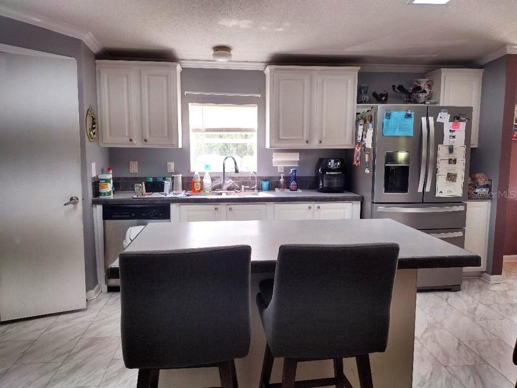 A kitchen features white cabinets, stainless steel appliances, a center island, and gray tile flooring — 1558 CANDLEBERRY STREET, BUNNELL, FL