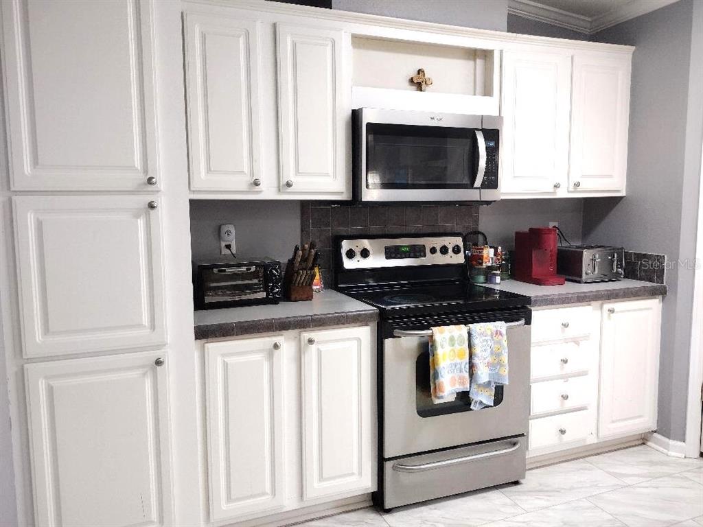 A kitchen features white cabinets, stainless steel appliances, and a dark tiled backsplash — 1558 CANDLEBERRY STREET, BUNNELL, FL