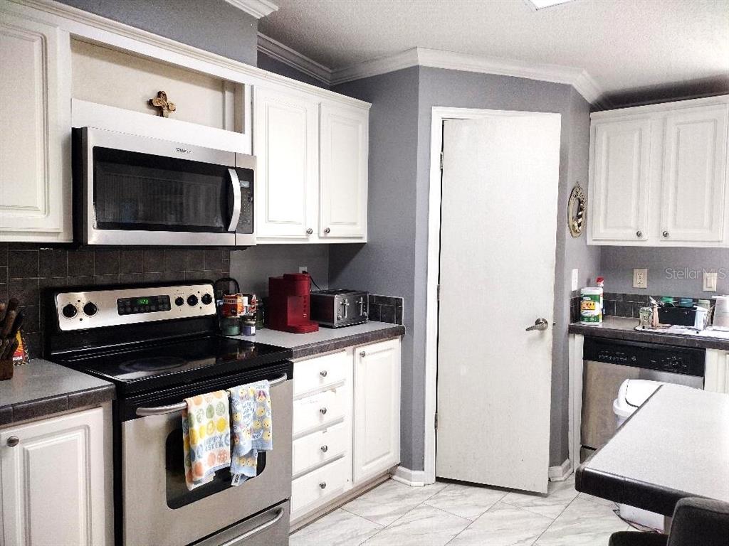 A kitchen features white cabinets, stainless steel appliances, gray walls, and light-colored tile flooring — 1558 CANDLEBERRY STREET, BUNNELL, FL