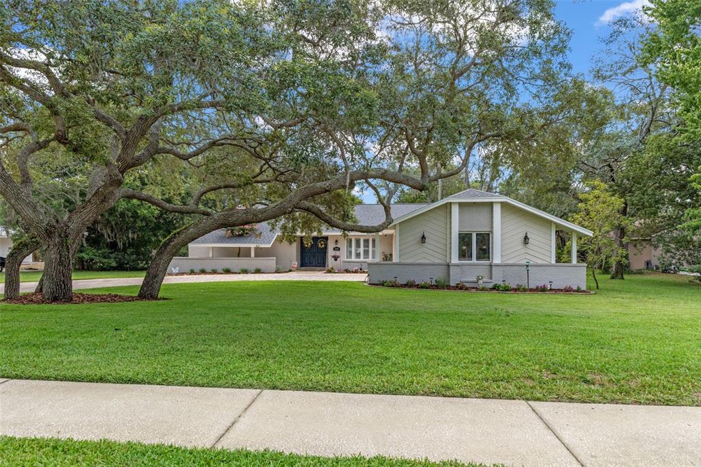 A single-story house with a light-colored exterior and large oak trees in the front yard — 5008 CUMBERLAND LANE, SPRING HILL, FL