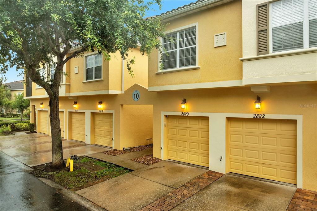 A row of yellow townhouses with garages and a large tree in the front yard — 2820 OAKWATER DRIVE UNIT 2820, KISSIMMEE, FL