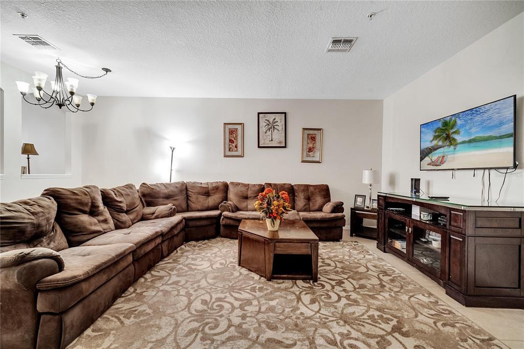 An open-concept living area features light tile flooring, a staircase, and a dining room chandelier — 2820 OAKWATER DRIVE UNIT 2820, KISSIMMEE, FL