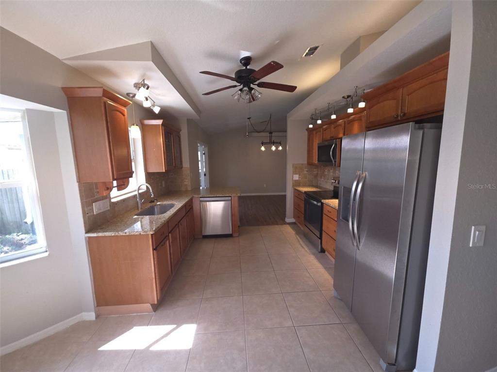 A kitchen features wood cabinets, granite countertops, stainless steel appliances, and tile flooring — 1002 TORGERSON STREET, NORTH PORT, FL