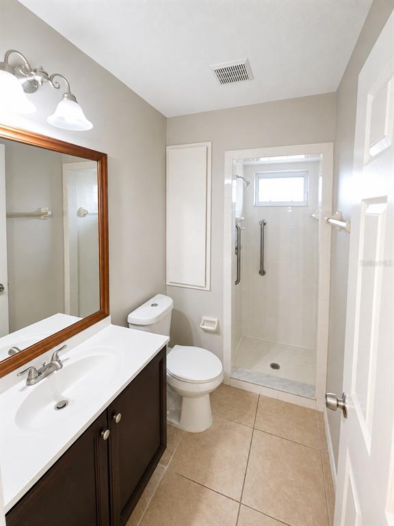 A bathroom features a dark wood vanity, a toilet, and a walk-in shower with grab bars — 1002 TORGERSON STREET, NORTH PORT, FL