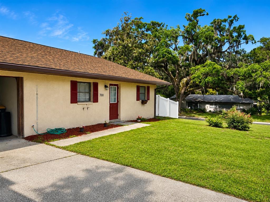 A single-story house with a tan stucco exterior, red shutters, and a red front door — 700 W DAMPIER STREET, INVERNESS, FL