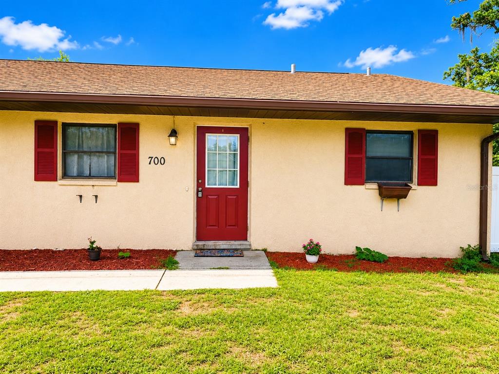 The exterior of a single-story house features a red front door and red window shutters — 700 W DAMPIER STREET, INVERNESS, FL