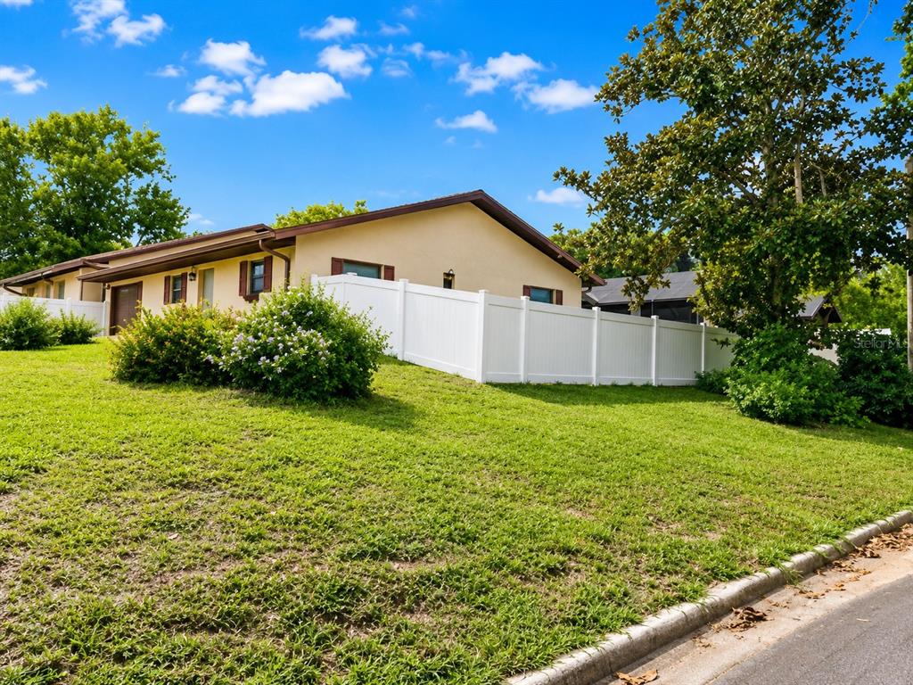 A tan house with a white vinyl fence sits on a grassy, sloped residential lot — 700 W DAMPIER STREET, INVERNESS, FL
