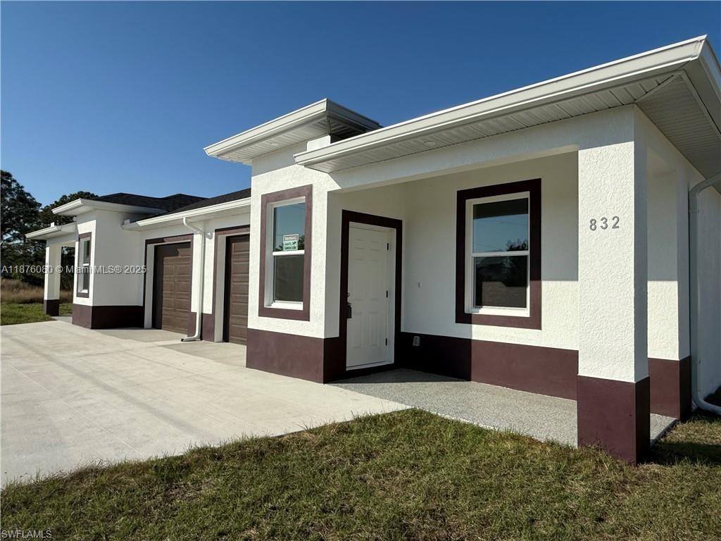 A white single-story house exterior features brown trim, a covered entryway, and two garage doors — 832 HOLMES AVE # 832, Lehigh Acres FL 33974, LEHIGH ACRES, FL