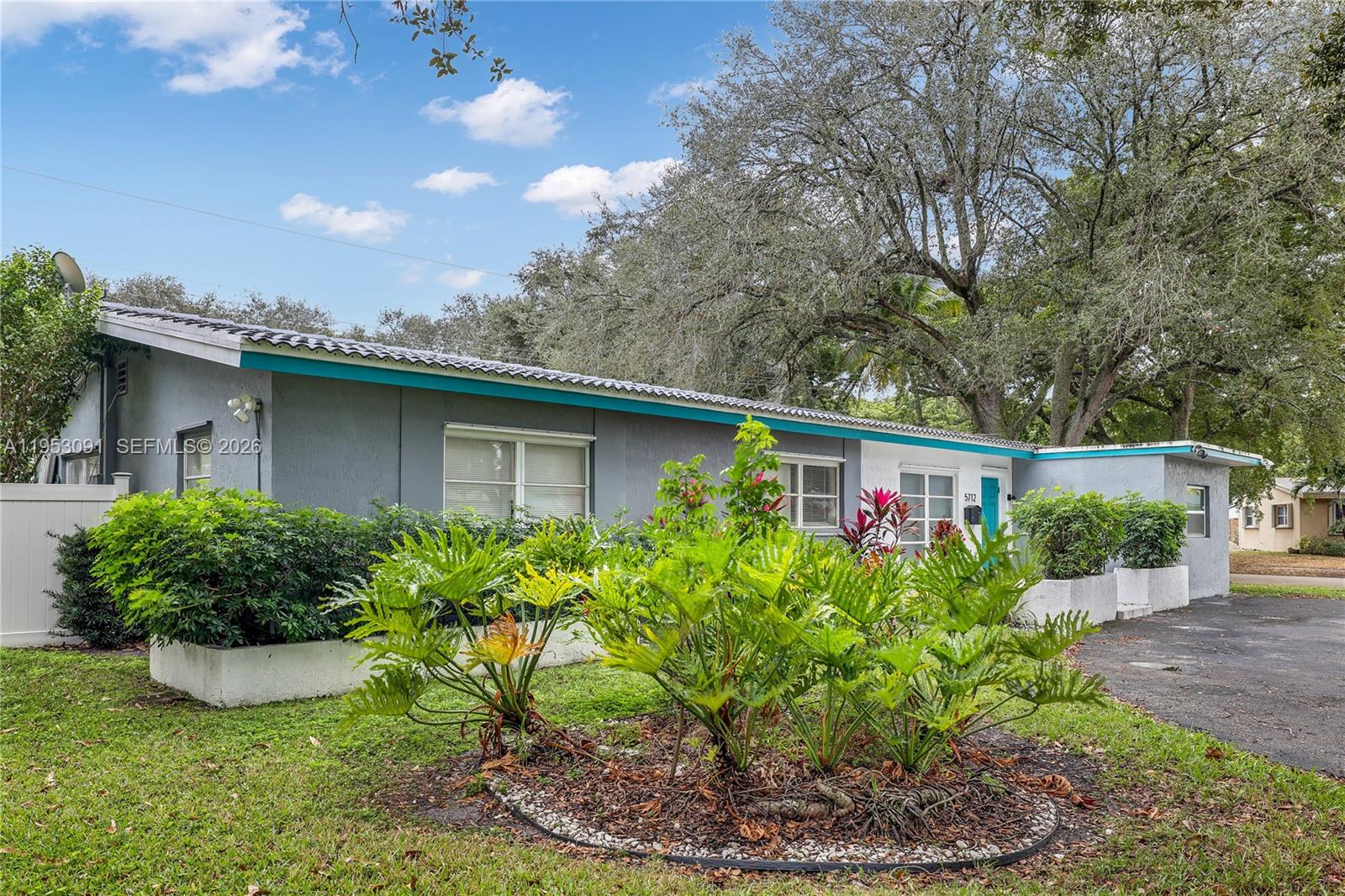 A single-story gray house features a teal trim, a paved driveway, and lush front landscaping — 5712 Monroe St, Hollywood FL 33023, HOLLYWOOD, FL