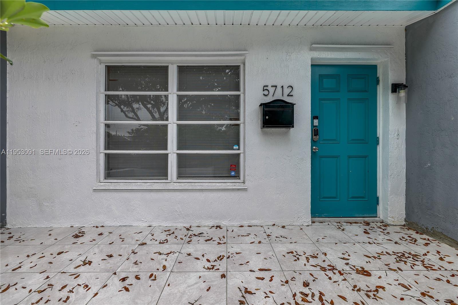 The exterior view shows a white stucco wall with a teal door and large window — 5712 Monroe St, Hollywood FL 33023, HOLLYWOOD, FL