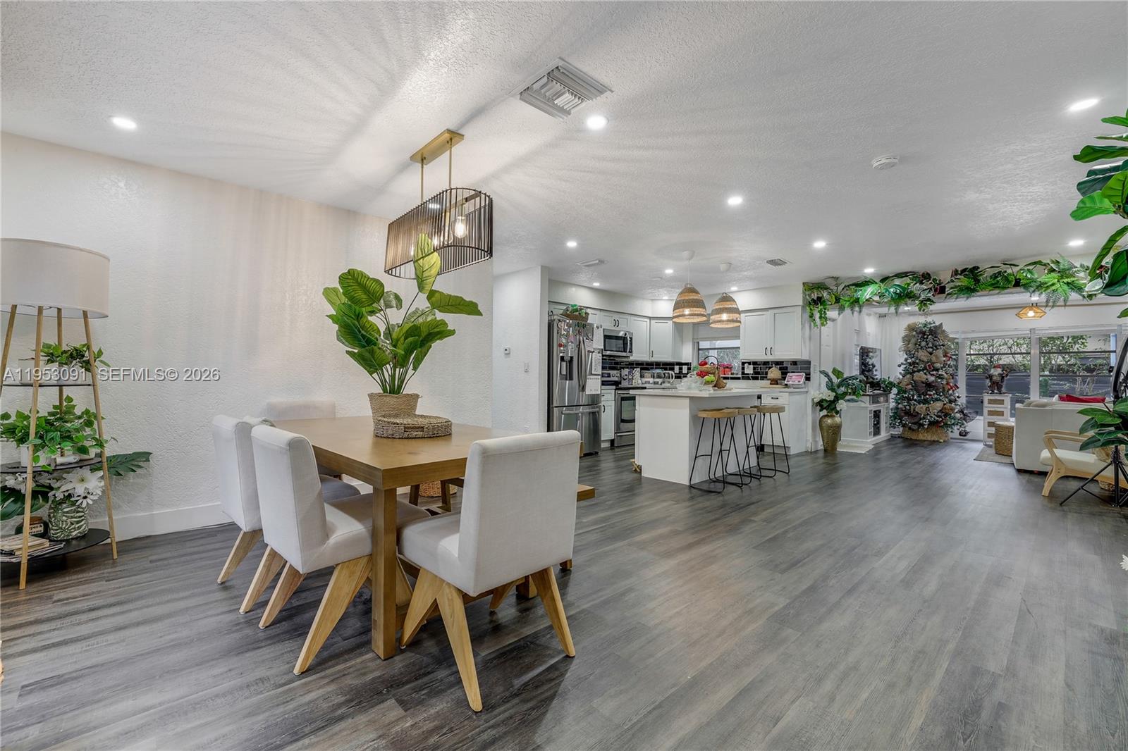 An open-concept dining area and kitchen feature wood-look flooring, white cabinetry, and modern lighting — 5712 Monroe St, Hollywood FL 33023, HOLLYWOOD, FL