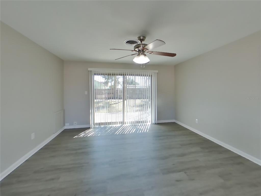 A living room features gray wood-look flooring, light walls, a ceiling fan, and sliding doors — 1122 IBSEN AVENUE, ORLANDO, FL