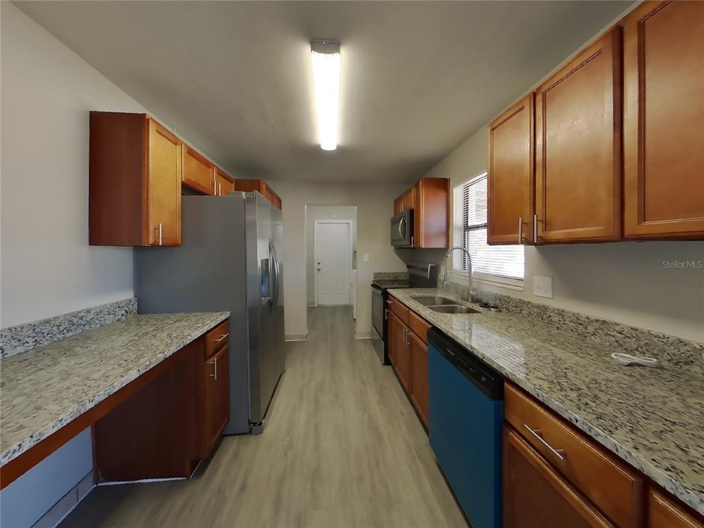 A galley kitchen features wood cabinets, granite countertops, stainless steel appliances, and light wood flooring — 1122 IBSEN AVENUE, ORLANDO, FL