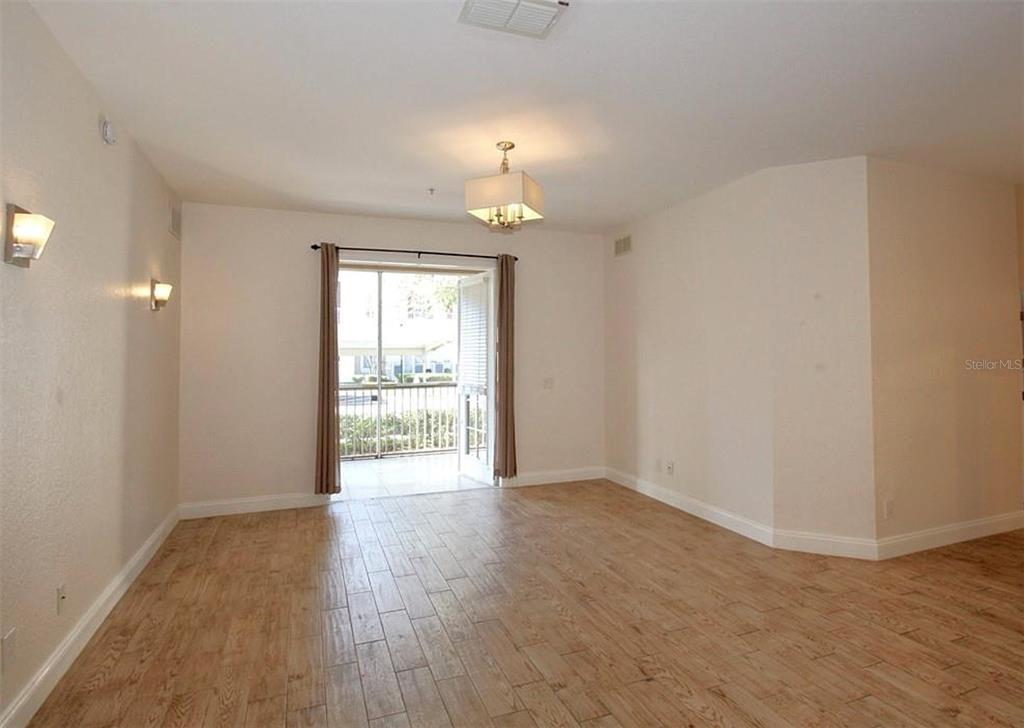An empty room with wood-look tile flooring, a central light fixture, and a balcony door — 3001 LAUREL PARK LANE UNIT 105, KISSIMMEE, FL