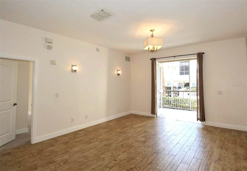 A room with light-colored walls, wood-look tile flooring, a chandelier, and a balcony door — 3001 LAUREL PARK LANE UNIT 105, KISSIMMEE, FL