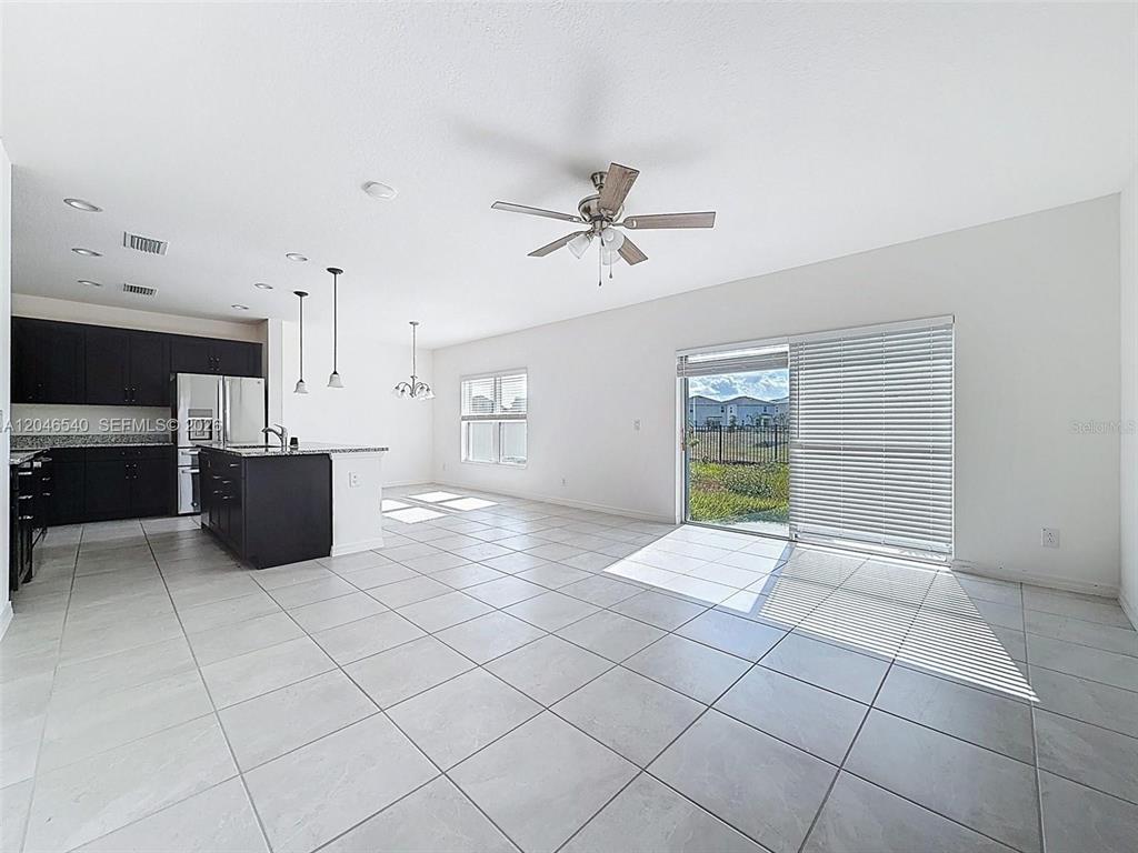 An open-concept kitchen and living area features white tile floors, dark cabinetry, and sliding doors — 857 SCRUB OAK HAMMOCK ROAD, DAVENPORT, FL