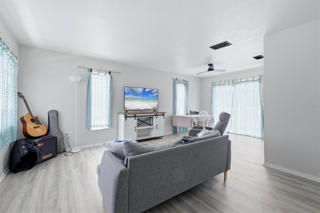 A living room features light wood-look flooring, a gray sofa, a television console, and curtains — 1805 MARBETH STREET UNIT 1805/1807, SARASOTA, FL