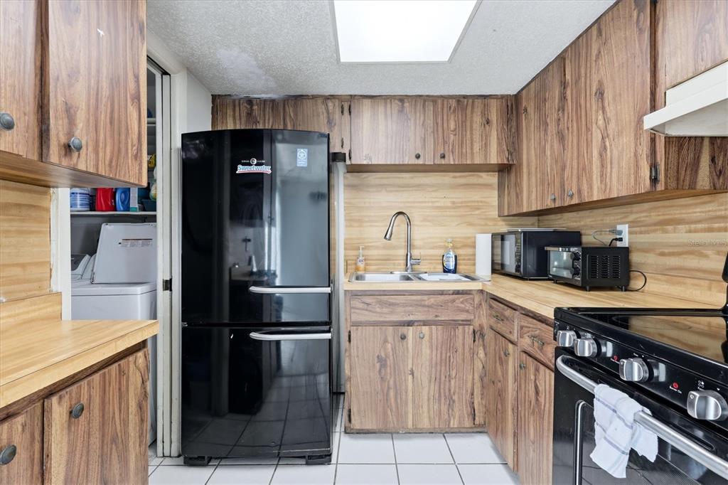A kitchen features wood-grain cabinets, a black refrigerator, a double sink, and white tile flooring — 1805 MARBETH STREET UNIT 1805/1807, SARASOTA, FL