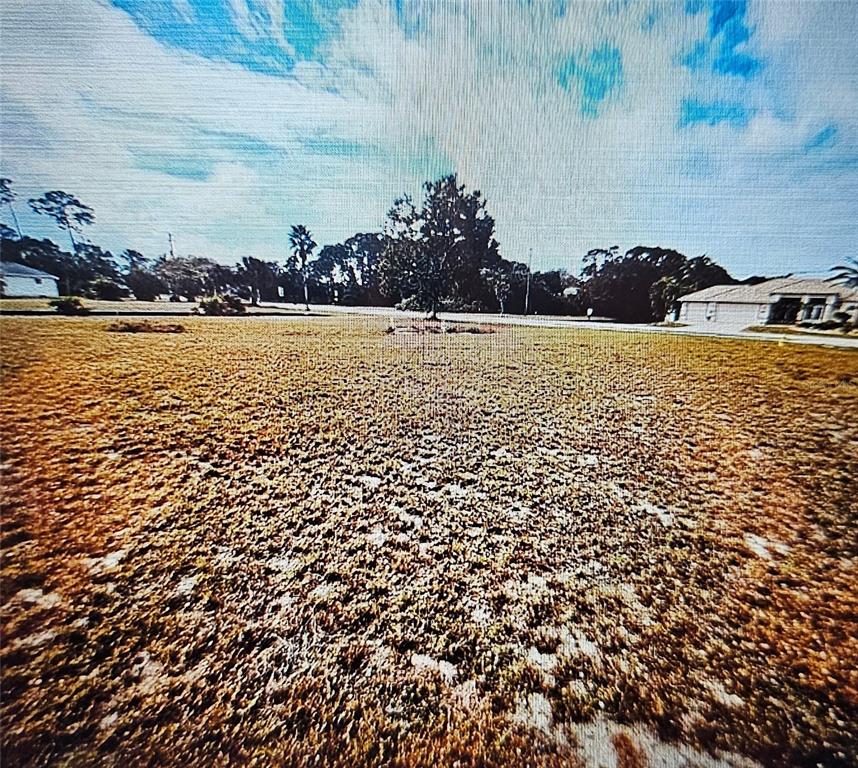 A wide, flat, grassy vacant lot is shown under a bright blue sky — 24283 PENHOLLOW COURT, PUNTA GORDA, FL