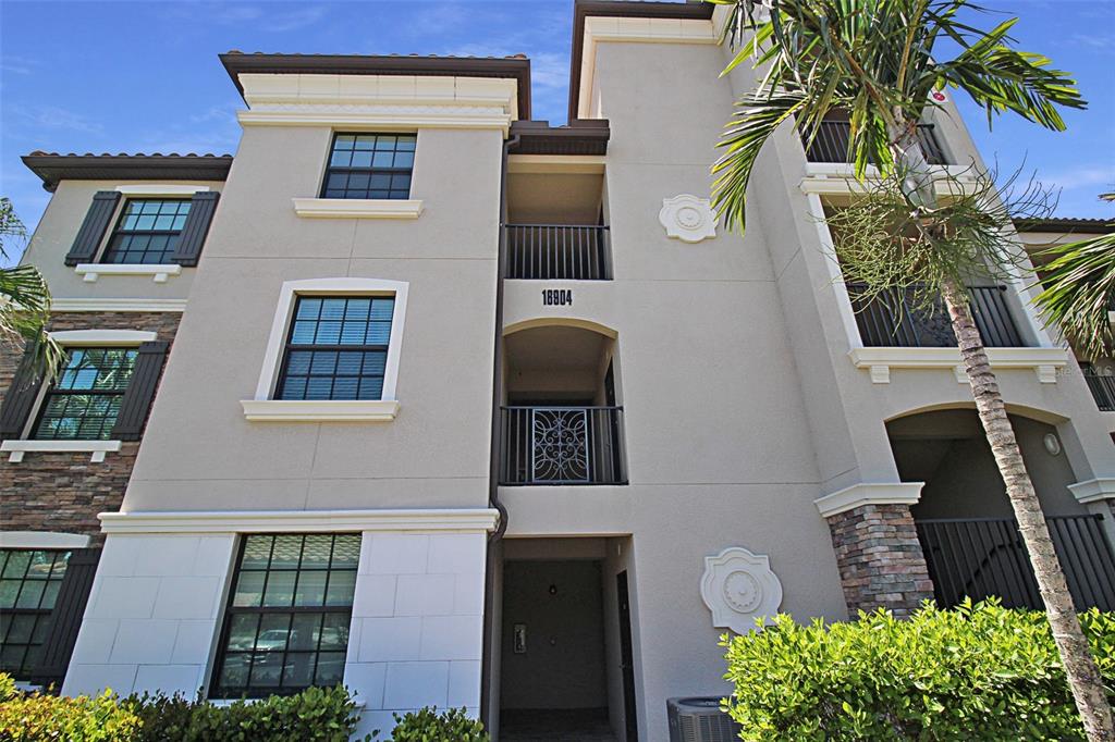A low-angle exterior view of a multi-story apartment building with balconies and stone accents — 16904 VARDON TERRACE UNIT 204, BRADENTON, FL