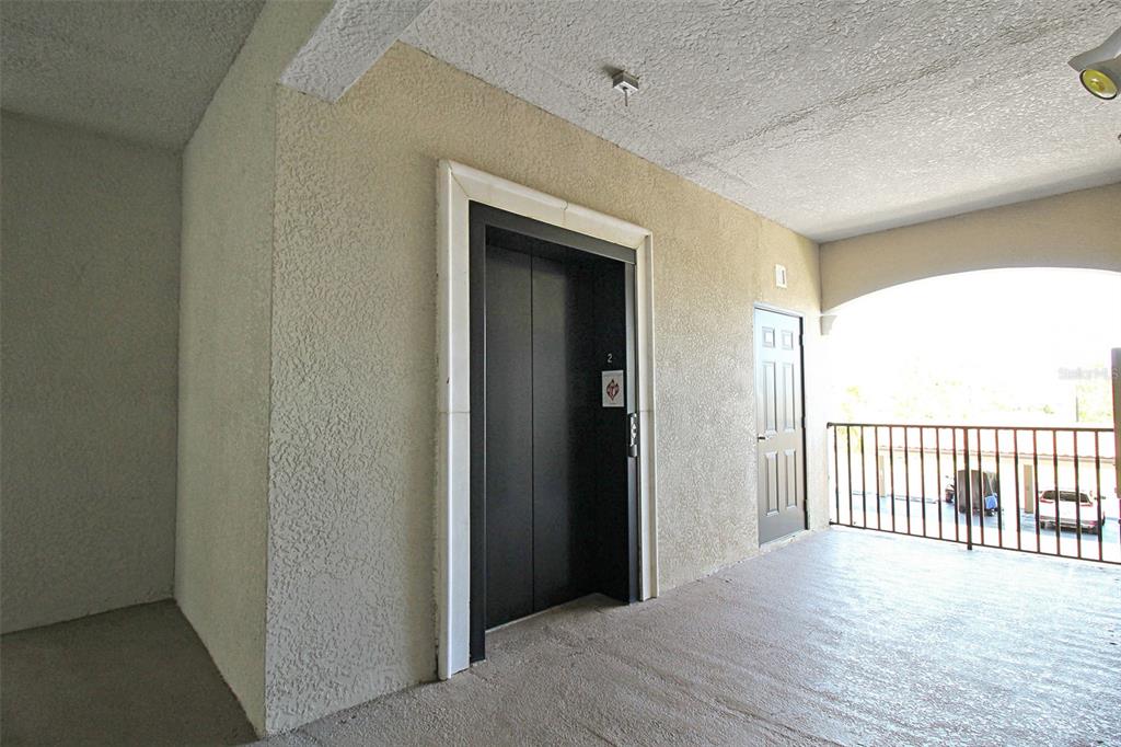 An outdoor elevator lobby features a black elevator door, a utility door, and a metal railing — 16904 VARDON TERRACE UNIT 204, BRADENTON, FL