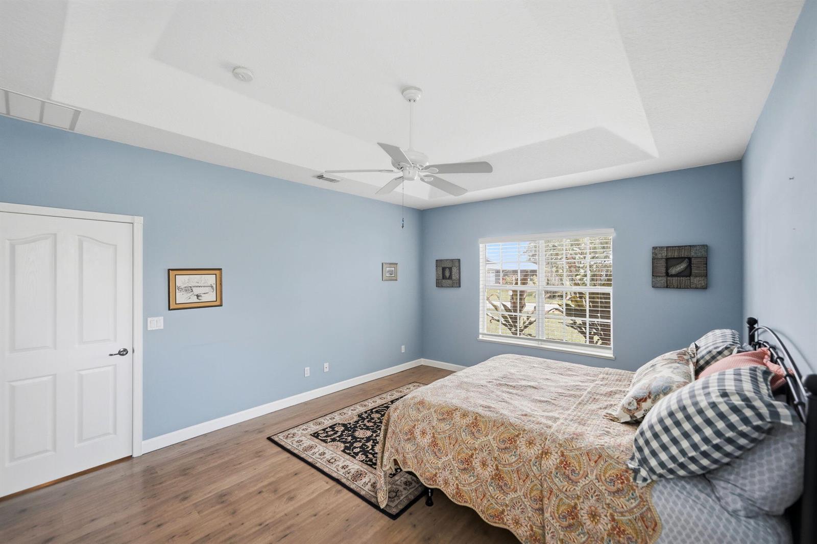 A bedroom with light blue walls, a tray ceiling, wood-look flooring, and a bed — 426 NE Vanda Terrado, Jensen Beach FL 34957, JENSEN BEACH, FL
