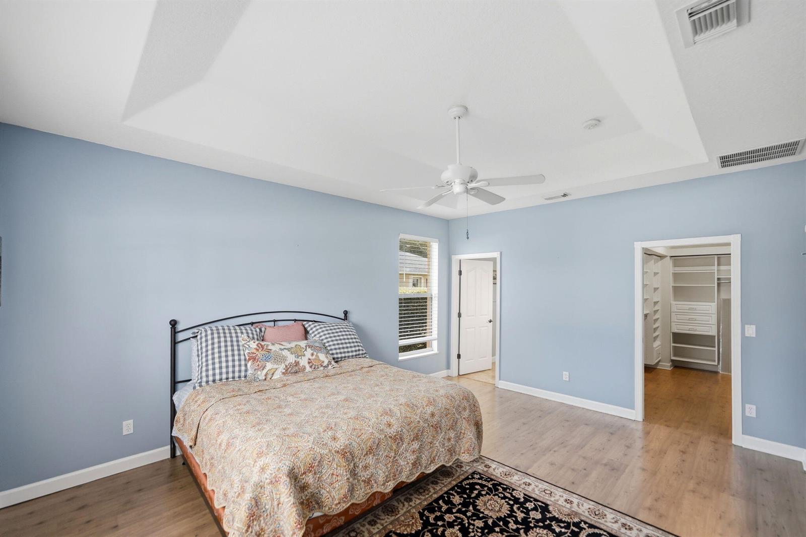 A bedroom with light blue walls, wood flooring, a tray ceiling, and a walk-in closet — 426 NE Vanda Terrado, Jensen Beach FL 34957, JENSEN BEACH, FL