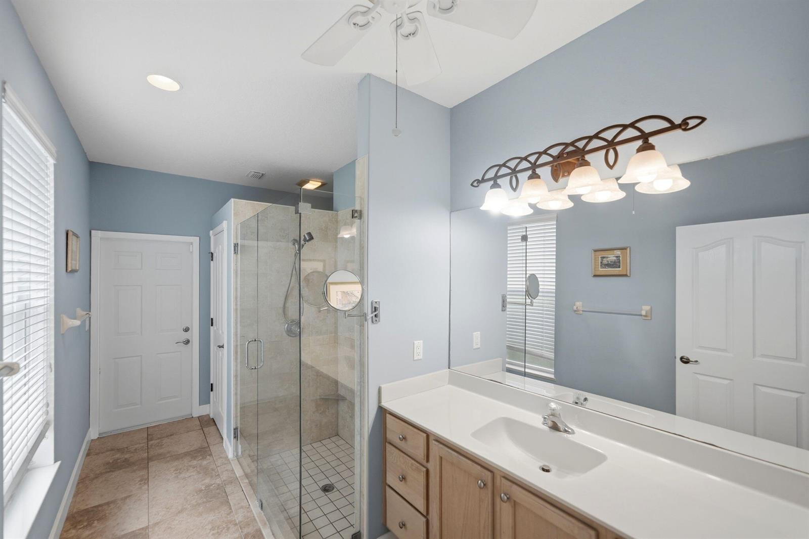 A bathroom features a glass-enclosed shower, a light wood vanity, and light blue walls — 426 NE Vanda Terrado, Jensen Beach FL 34957, JENSEN BEACH, FL