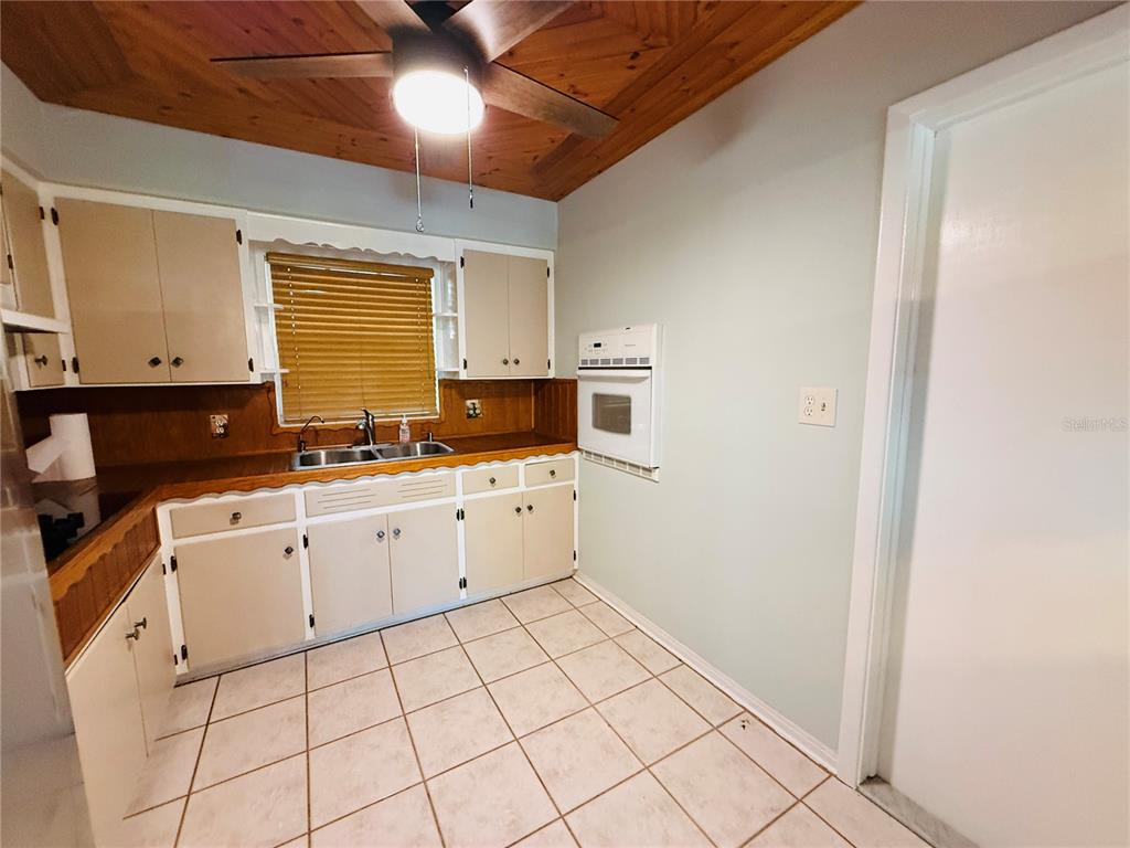 A kitchen features light-colored cabinets, a wood-paneled ceiling, tiled flooring, and a built-in oven — 11537 63RD AVENUE, SEMINOLE, FL