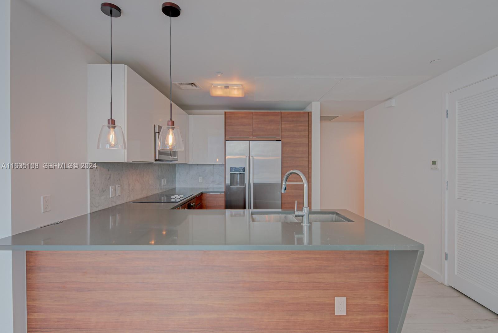 A modern kitchen features a gray countertop island, wood-toned cabinetry, and white upper cabinets — 601 NE 27th St # 1502, Miami FL 33137, MIAMI, FL