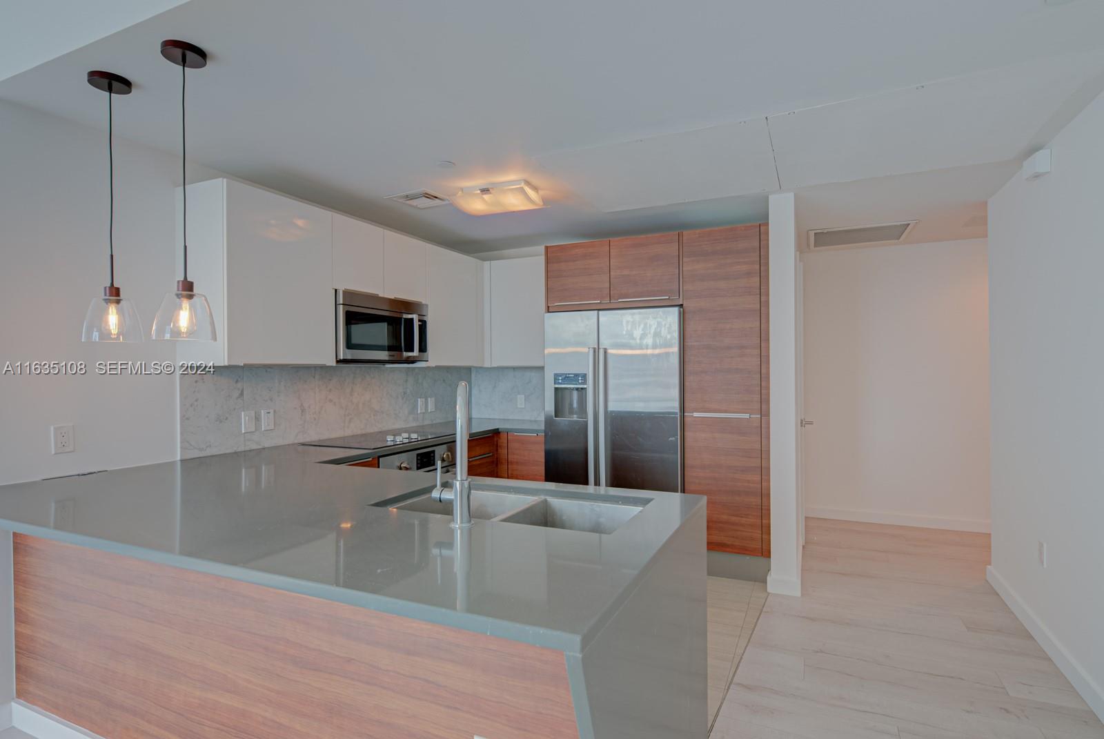 A modern kitchen features white and wood-toned cabinetry, stainless steel appliances, and a gray countertop — 601 NE 27th St # 1502, Miami FL 33137, MIAMI, FL