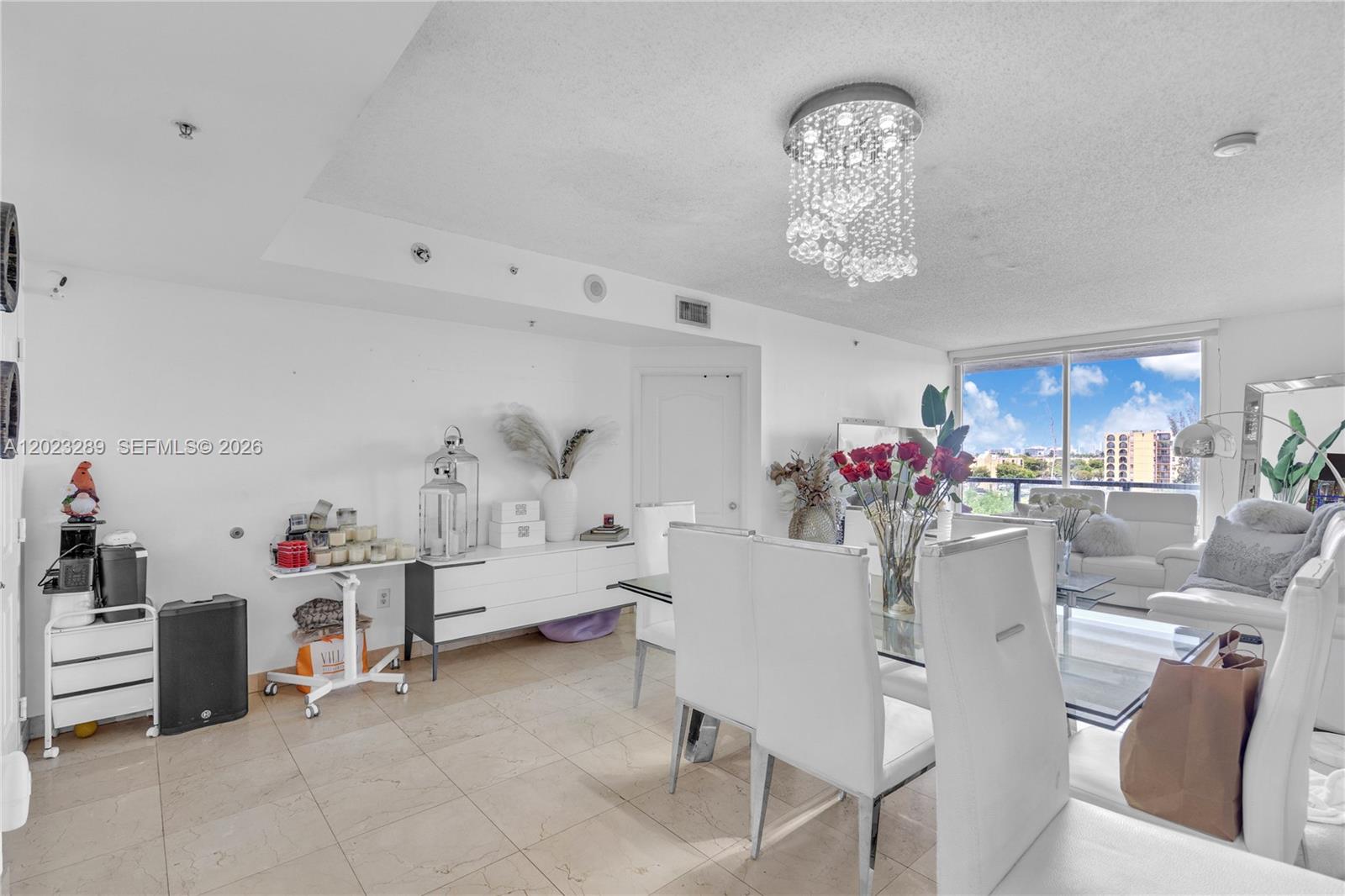 A bright dining and living area features white furniture, a crystal chandelier, and tile flooring — 5077 NW 7th St # 517, Miami FL 33126, MIAMI, FL
