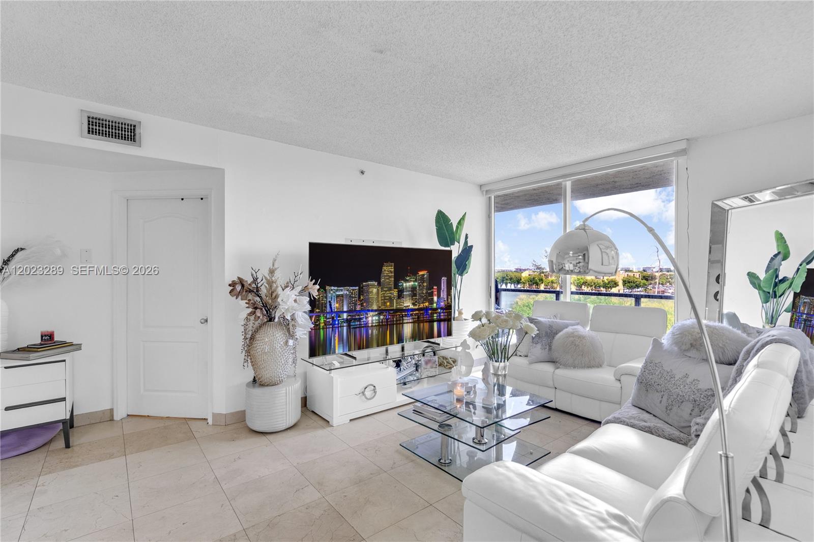 A bright living room features white leather sofas, a glass coffee table, and a television — 5077 NW 7th St # 517, Miami FL 33126, MIAMI, FL