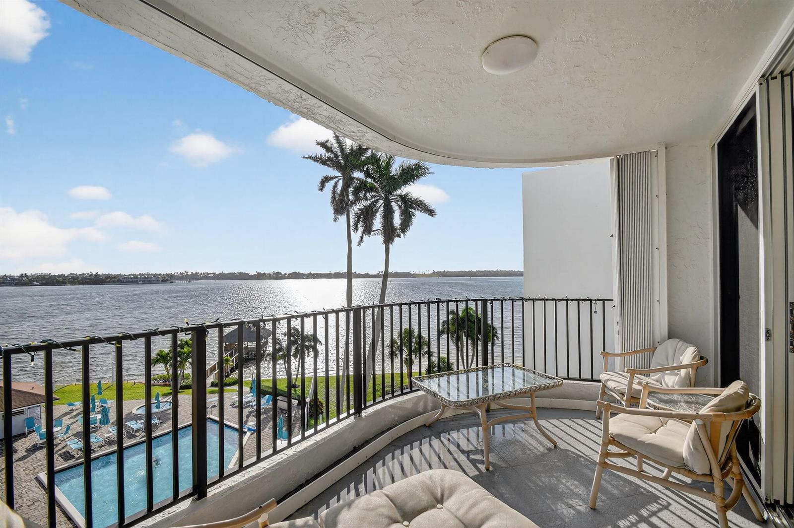 A balcony with patio furniture overlooks a swimming pool and a large body of water — 8200 Lakeshore Drive # 507, Hypoluxo FL 33462, HYPOLUXO, FL