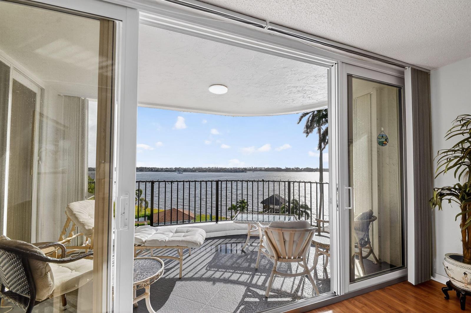 A balcony with outdoor furniture overlooks a large body of water through sliding glass doors — 8200 Lakeshore Drive # 507, Hypoluxo FL 33462, HYPOLUXO, FL