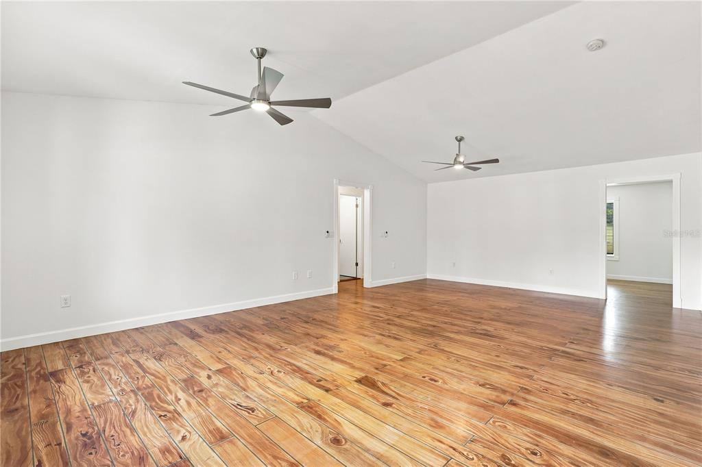 A spacious room with white walls, vaulted ceilings, two ceiling fans, and wood-look flooring — 5825 ALSTRUM DRIVE, PORT ORANGE, FL