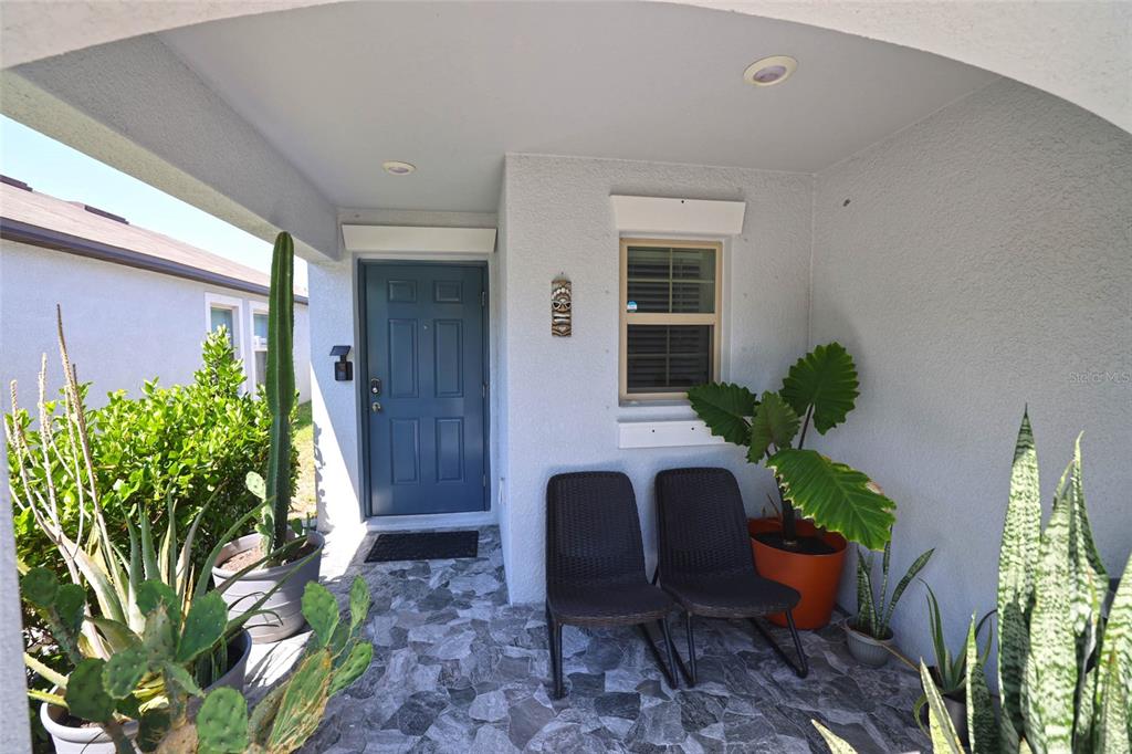 A covered front porch features a blue door, two wicker chairs, and several potted plants — 16761 DELIA STREET, WIMAUMA, FL