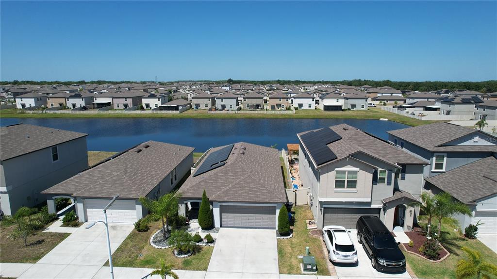 An aerial view shows suburban houses with solar panels and a pond in the background — 16761 DELIA STREET, WIMAUMA, FL