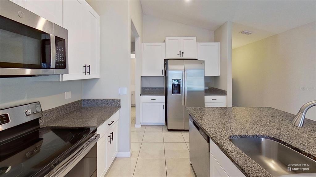 A kitchen featuring white cabinets, granite countertops, stainless steel appliances, and light tile flooring — 16761 DELIA STREET, WIMAUMA, FL