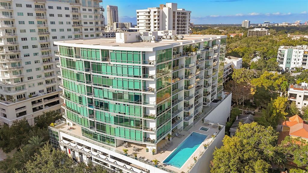 An aerial view shows a modern glass-walled apartment building with an outdoor swimming pool — 101 S EOLA DRIVE UNIT 1203, ORLANDO, FL