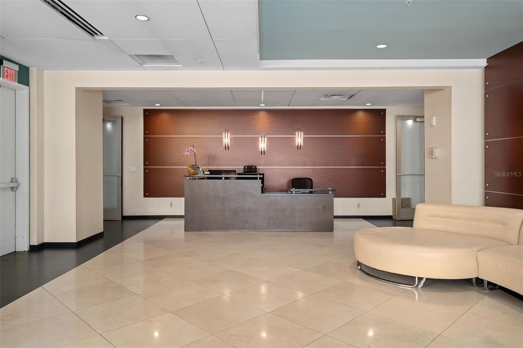 A modern office reception area features a dark desk, wood-paneled wall, and curved beige sofa — 101 S EOLA DRIVE UNIT 1203, ORLANDO, FL