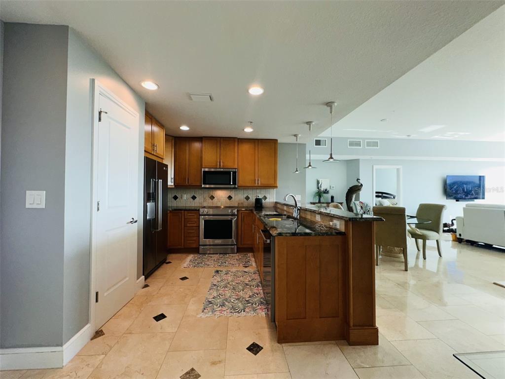 A kitchen with wood cabinets, granite countertops, and stainless steel appliances opens to a living area — 101 S EOLA DRIVE UNIT 1203, ORLANDO, FL