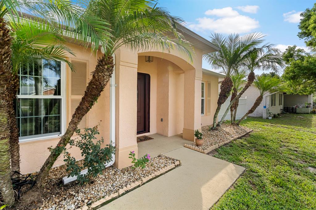 A peach-colored house exterior features a covered entryway, palm trees, and a concrete walkway — 640 FAIRHAVEN STREET, DELTONA, FL