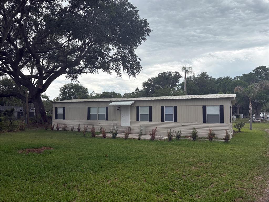 A single-story manufactured home with tan siding sits on a grassy lot under trees — 3923 WARD ROAD, LAKELAND, FL