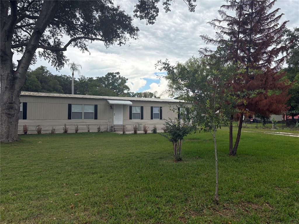 A single-story manufactured home sits on a grassy lot with trees under a cloudy sky — 3923 WARD ROAD, LAKELAND, FL