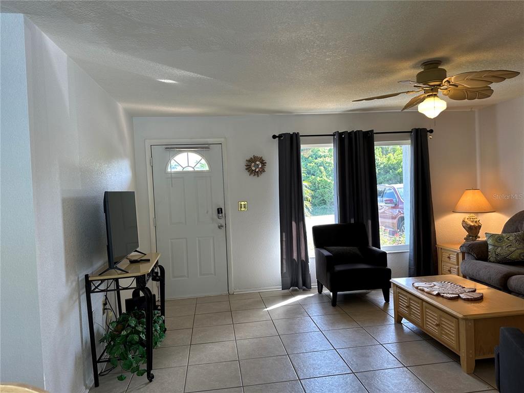 A living room features tile flooring, a front door, a television, and a ceiling fan — 18625 ALPHONSE CIRCLE, PORT CHARLOTTE, FL